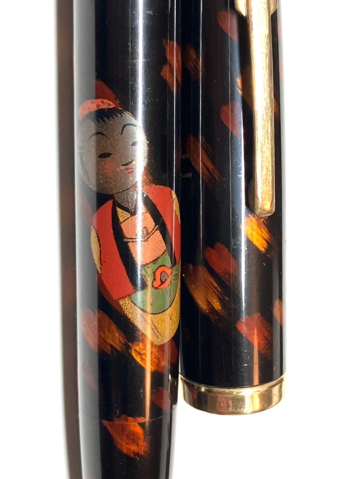 Black vintage fountain pen with gold tip, featuring colorful Japanese kokeshi figure in red, green, and yellow attire on barrel.