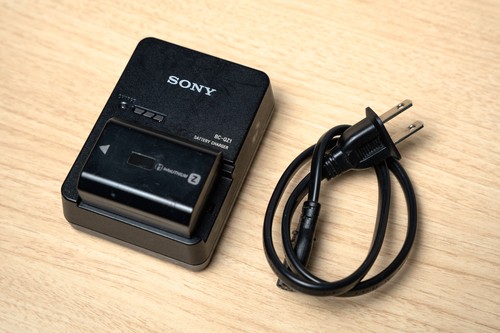 Black Sony Alpha a7S III body with two batteries, charger, and power cord on wooden surface.