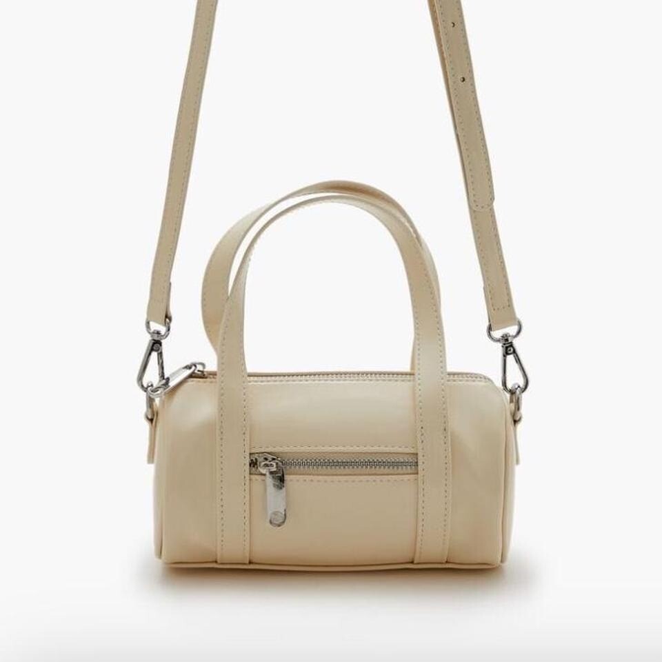 Cream mini cylinder bag with silver hardware, featuring a zip closure