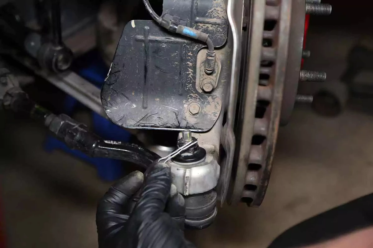 A mechanic removes the cotter pin from the lower ball joint’s castle nut.