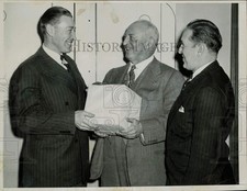 Press Photo Dit Clapper giving a gift to a man with another man watching
