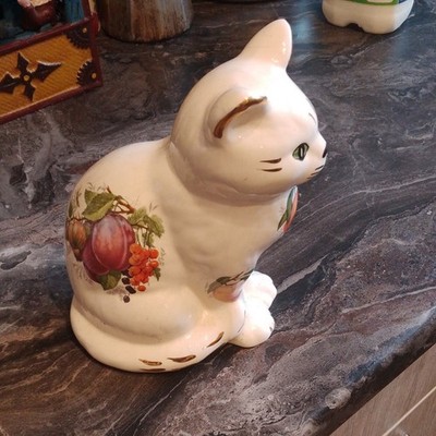 Sitzende weiße Keramik Katze Ornament mit Obst & Laub darauf bemalt.