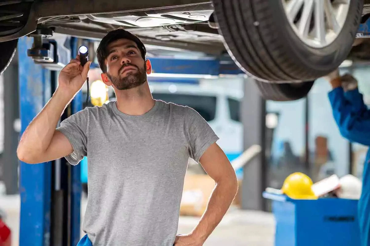 A technician looks underneath a car, using a flashlight.