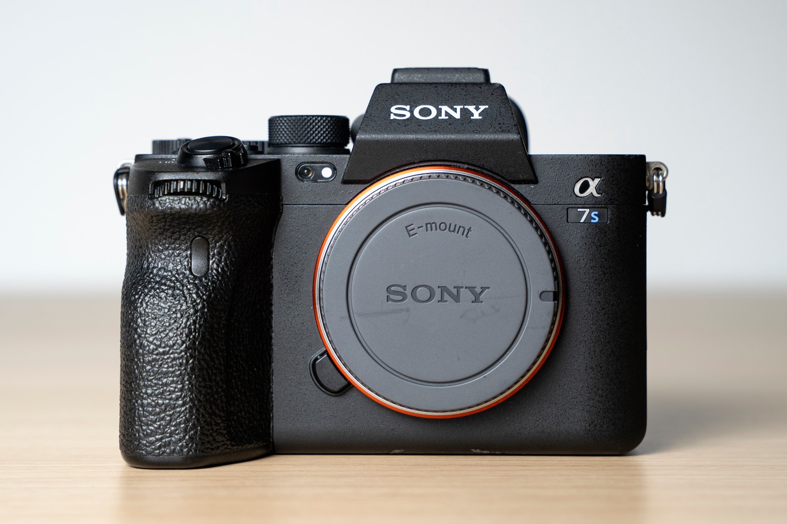 Black Sony Alpha a7S III camera with orange E-mount, textured grip, and two black batteries on a wooden surface.