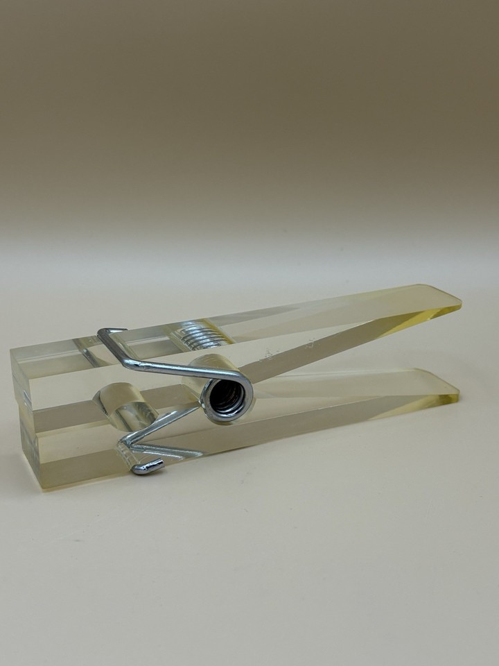 A giant Lucite clothespin repurposed as a MCM paperweight — absurdist, functional, and weirdly perfect on a creative's desk.