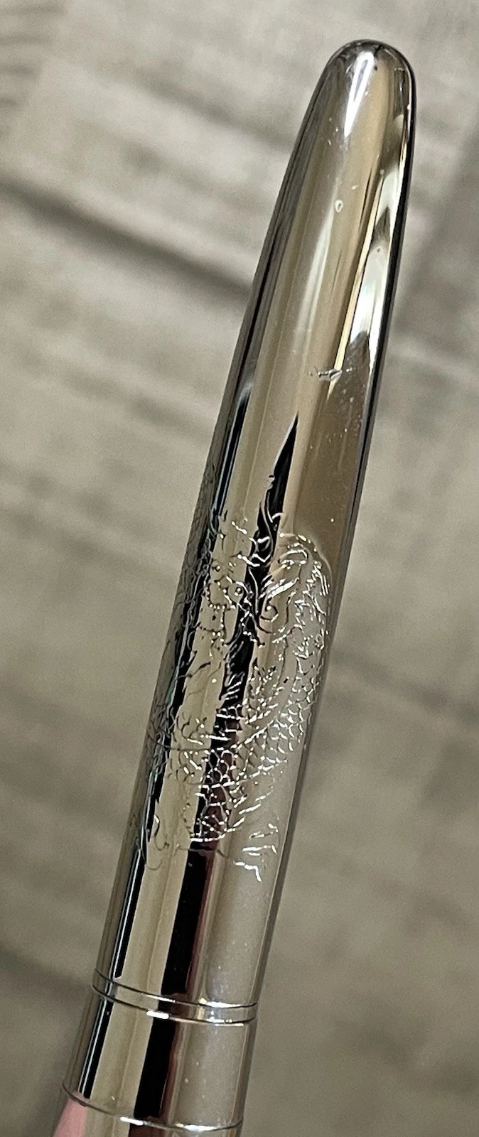 Chrome-plated Pilot Namiki fountain pen with fine nib, engraved with dragon and cloud design on textured barrel.