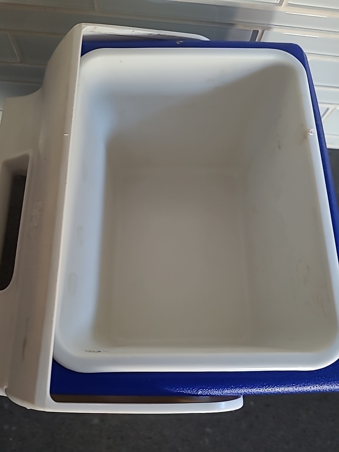 White rectangular Igloo Playmate cooler with black top and blue sides, made in USA, on a dark granite countertop.
