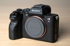 Black Sony Alpha a7S III body with silver accents, front screen, and two black batteries on a wooden surface.
