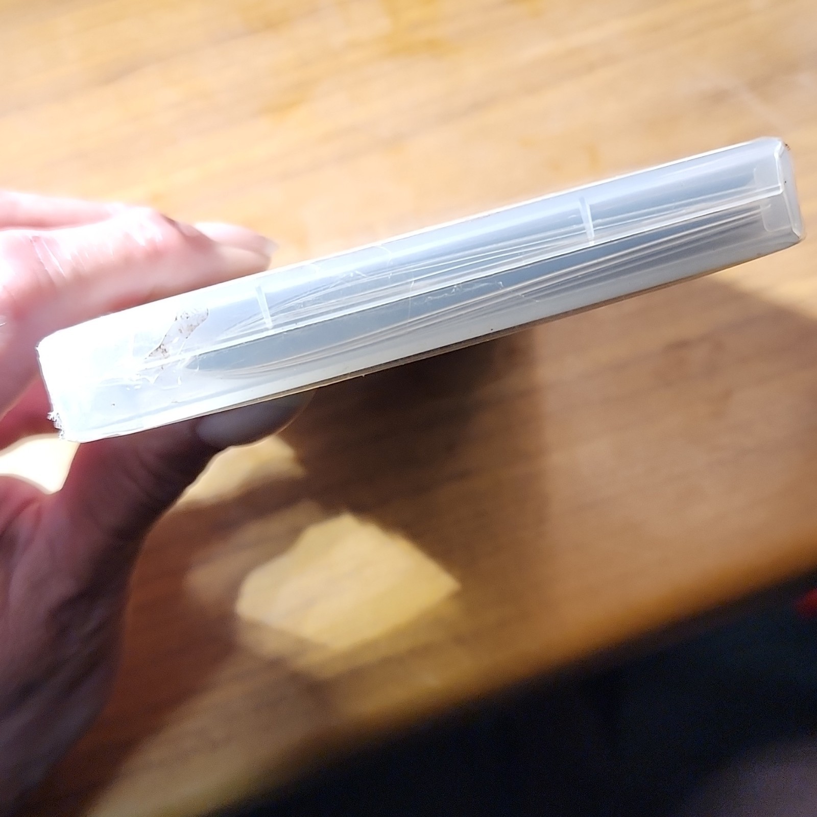 White Namco Ridge Racers 2 Sony PSP case with black horizontal stripes, held in a hand against a wooden surface.