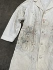 White vintage painters smock with visible paint stains, button front, and two large front pockets on a gray surface.