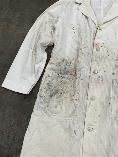 White vintage painters smock with visible paint stains, button front, and two large front pockets on a gray surface.