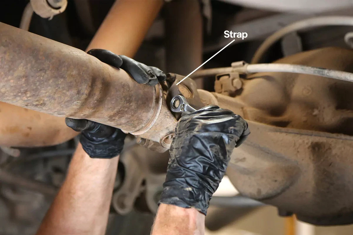 A mechanic wearing black gloves uses a wrench to tighten the bolt that secures the U-joint to the pinion yoke.