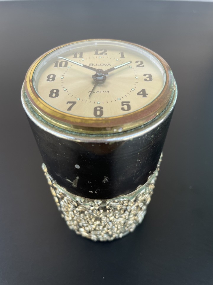 A German-made Bulova gold filigree travel clock that moonlights as a vanity cosmetics holder — tiny, ornate, and impossibly glamorous.