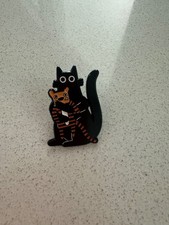small black cat pin holding a stuffed tiger