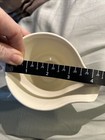 Cream ceramic bowl with black rim, marked in inches, holding a hand measuring against a light gray background.