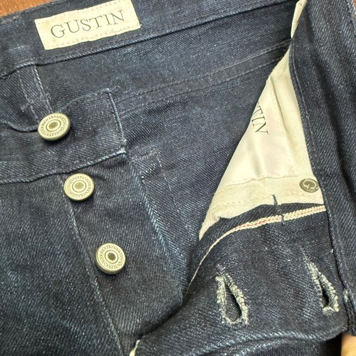 Front pockets, button closure, and white “Gustin” label inside waistband of blue denim jeans.