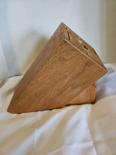 Cutco solid honey oak wood knife storage block with 13 slots, resting on a white fabric surface.