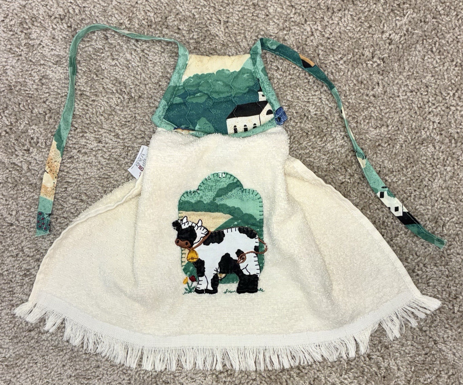 White vintage cotton kitchen towel with green cow and tree applique, red farmhouse VTG label, and blue fringe trim.
