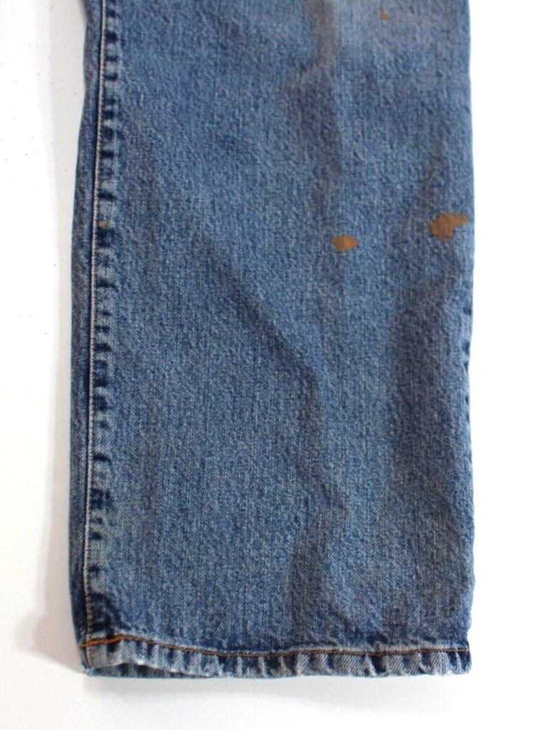 Blue medium wash jeans with brown paint splatter on left leg, white stitching, and “Lucky Brand” label on waistband.