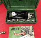 Green carry-case with black Singer 160506 buttonholer, white dial, and red box labeled “Singer Buttonholer Made in U.S.A.”