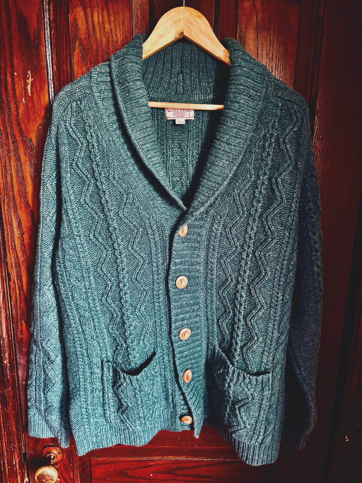 Teal green chunky cable-knit shawl collar cardigan with patch pockets, shown on a hanger.
