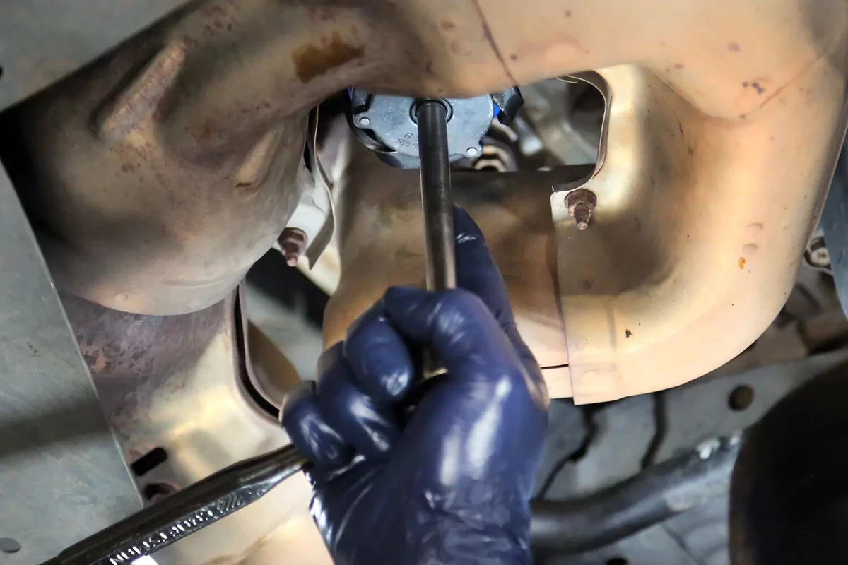 Hand holding a wrench on an oil filter under a vehicle.