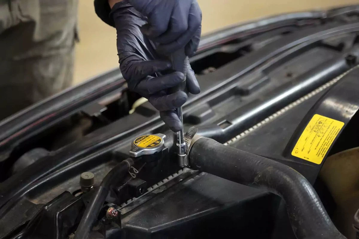 A mechanic uses a nut driver on a radiator hose clamp.