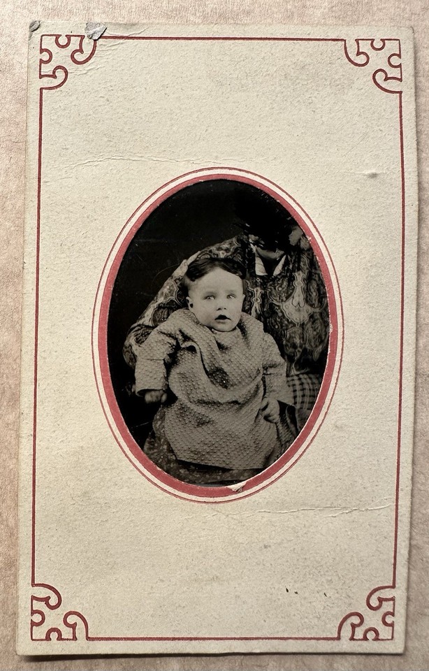 An 1870s tintype where the mother is completely hidden under fabric to keep the baby still — faceless, eerie, and a genuine Victorian photographic artifact.