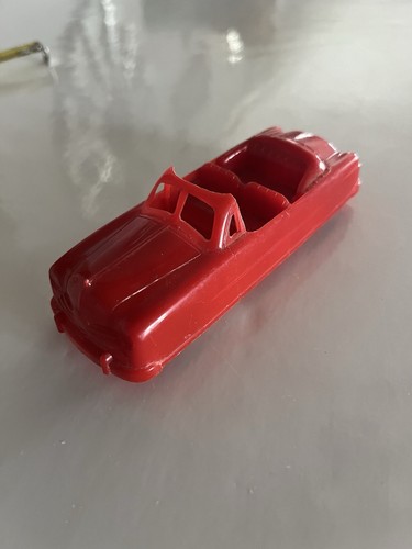 Red vintage 1950s BHS plastic convertible car with black seats, made in the USA on a reflective surface.