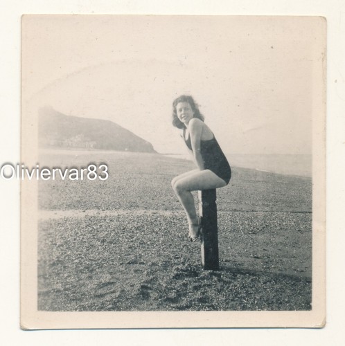 Vintage photo - young woman in swimsuit sitting on a pole on a beach