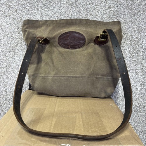 Brown canvas crossbody bag with dark brown leather strap, brass rivets, and stitched leather handles on a wooden surface.