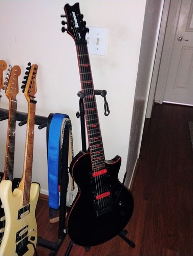 Black Kramer Assault electric guitar with red and white Floyd Rose, coil tap, and 24 frets on stand against white background.