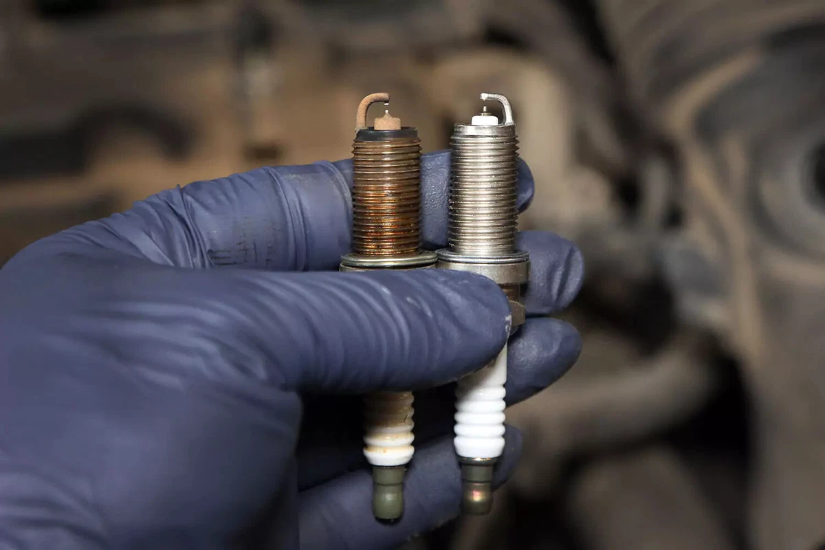 An old spark plug held up next to a new one.
