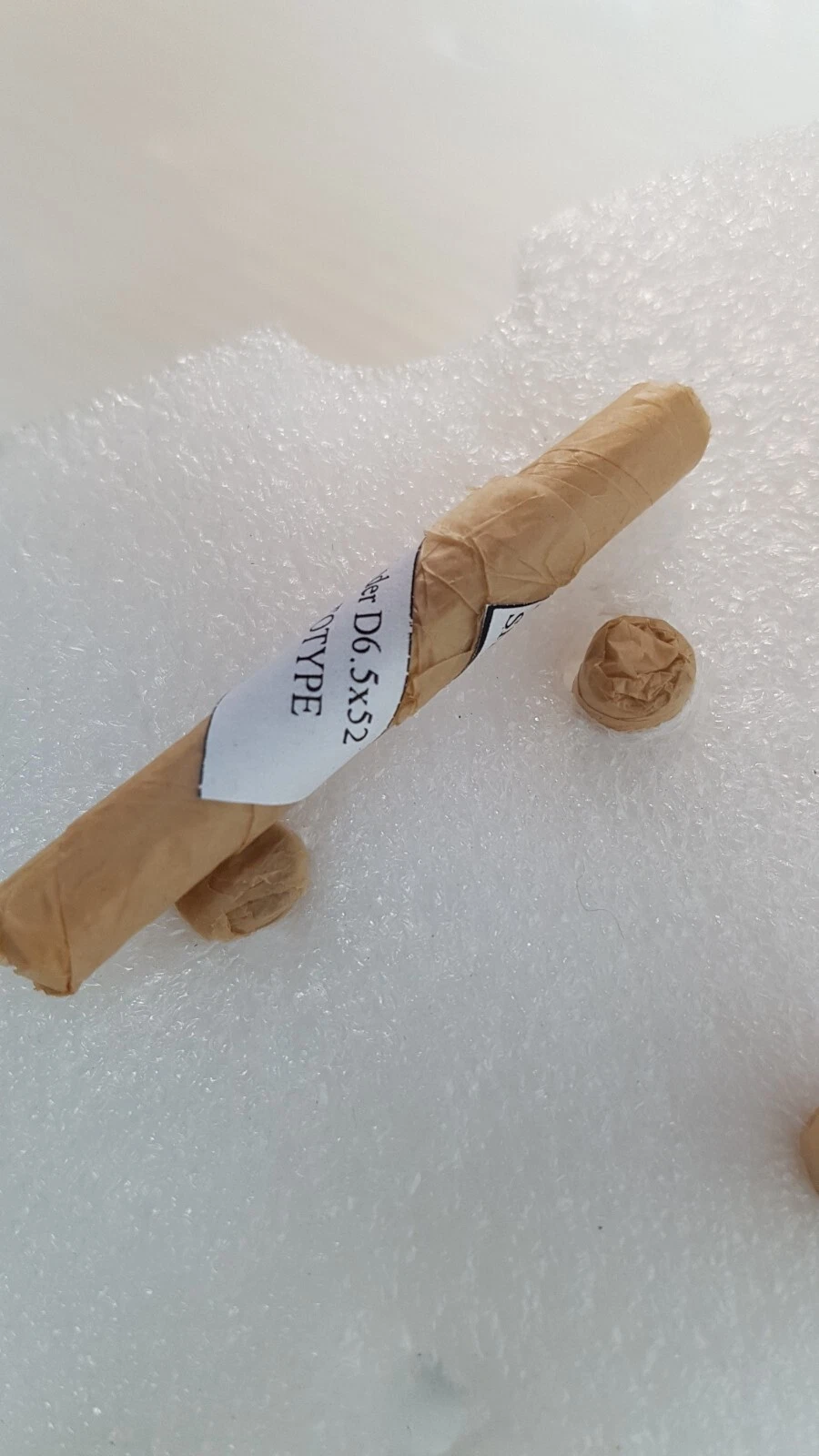 Wrapped sapphire cylinder labelled Cylinder D6.5x52 PROTOTYPE on white foam
