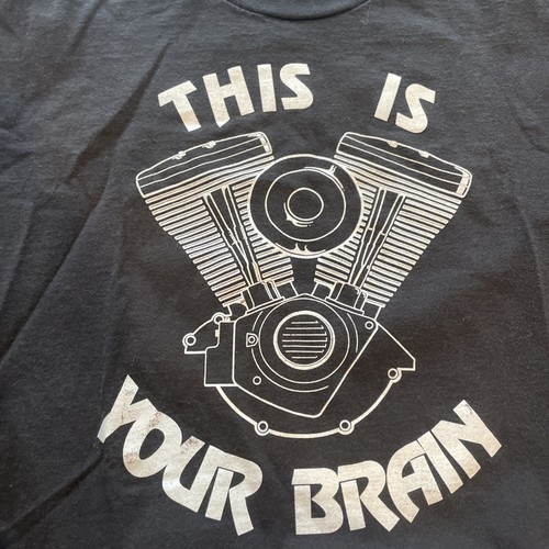 Black t-shirt with white outline of a motorcycle engine and the text “THIS IS YOUR BRAIN ON DRUGS” MADE IN USA.
