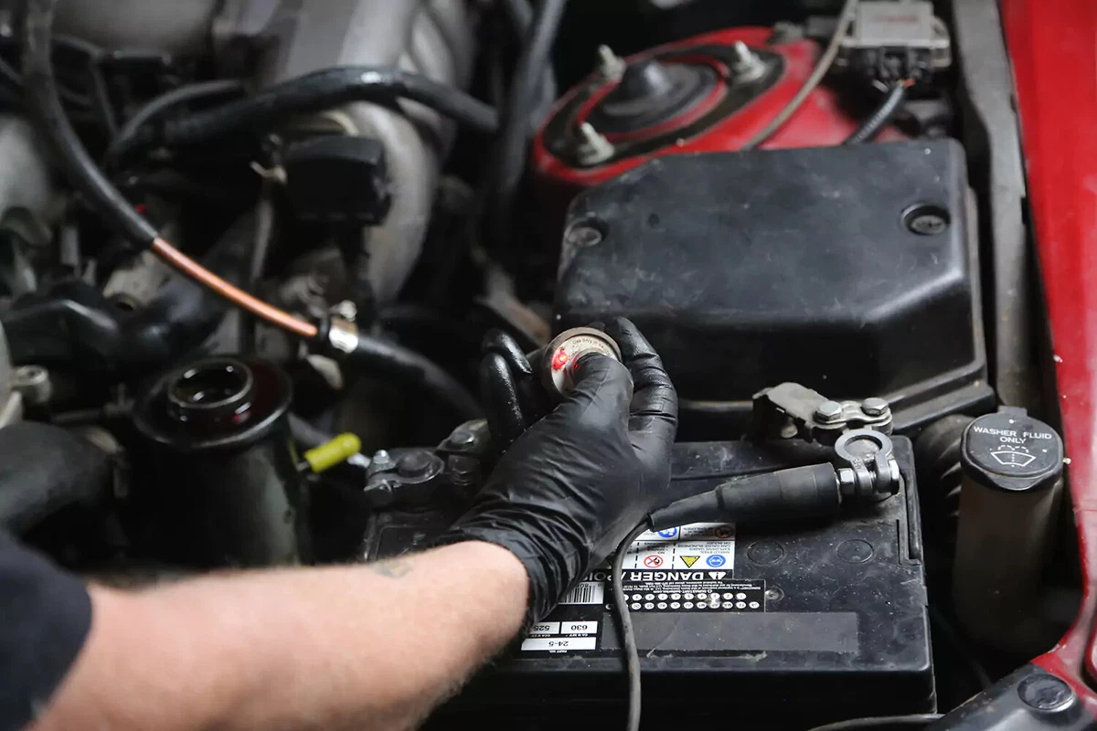 A mechanic wearing a black glove presses a bump starter's button to crank the vehicle's engine.