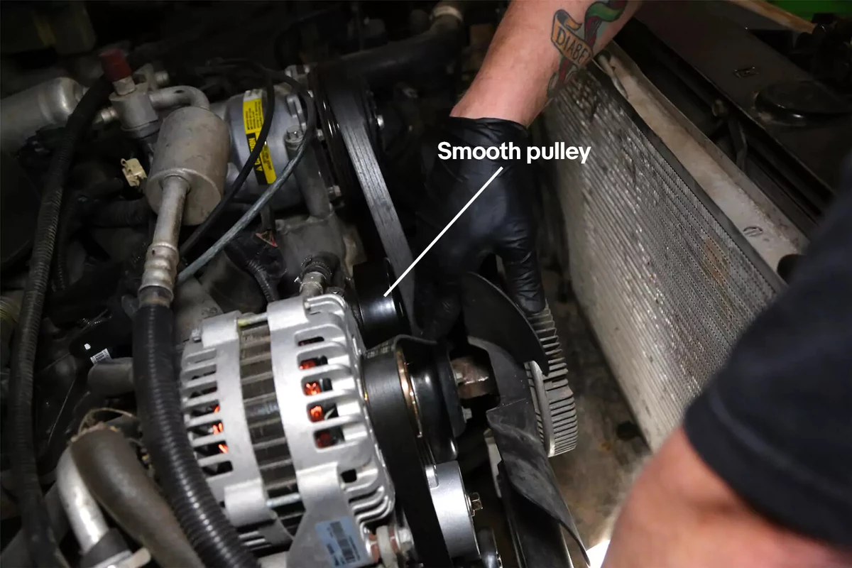 A mechanic wearing black gloves routes the serpentine belt through the new tensioner.