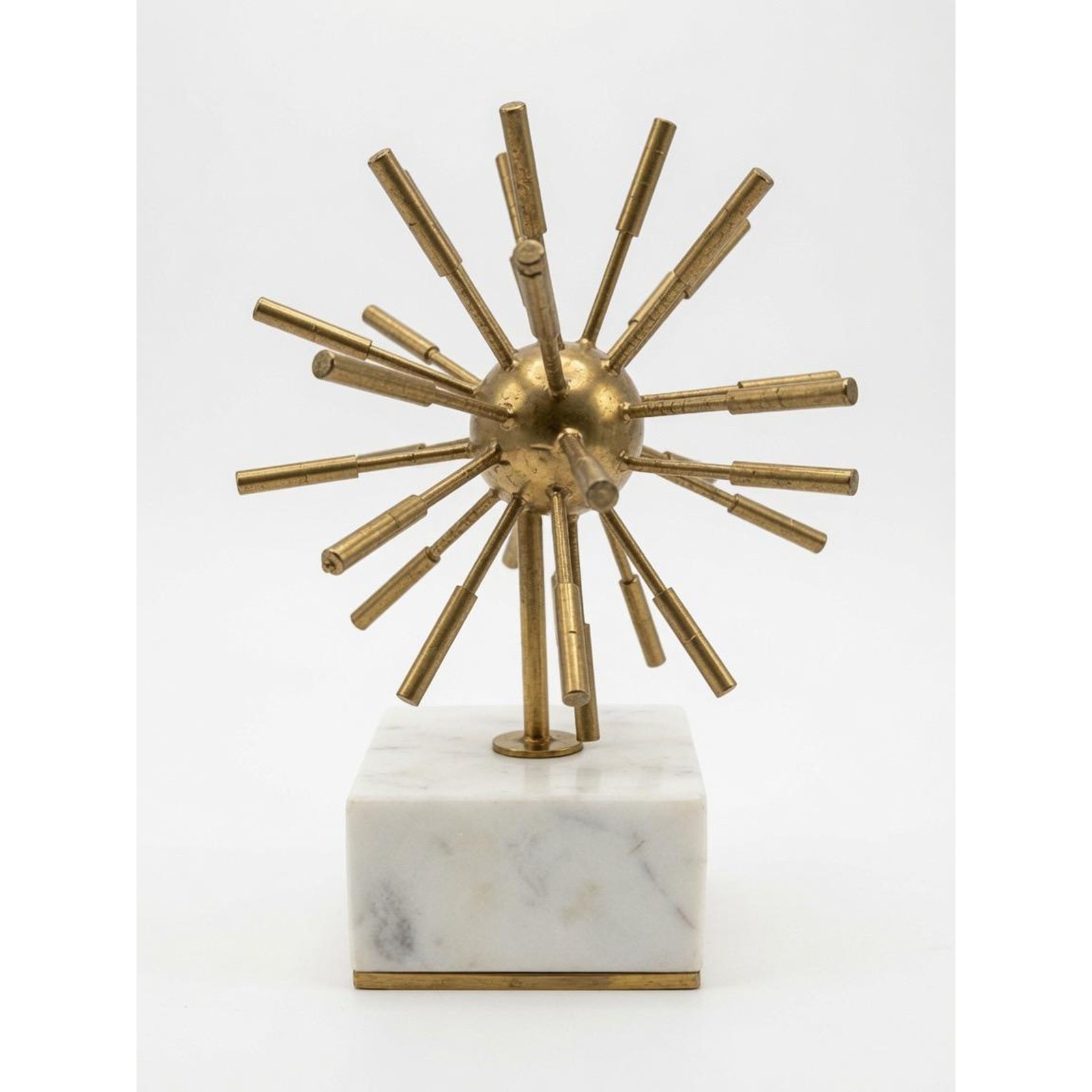 A brass starburst sculpture with radiating spiked rays mounted on a white marble base.