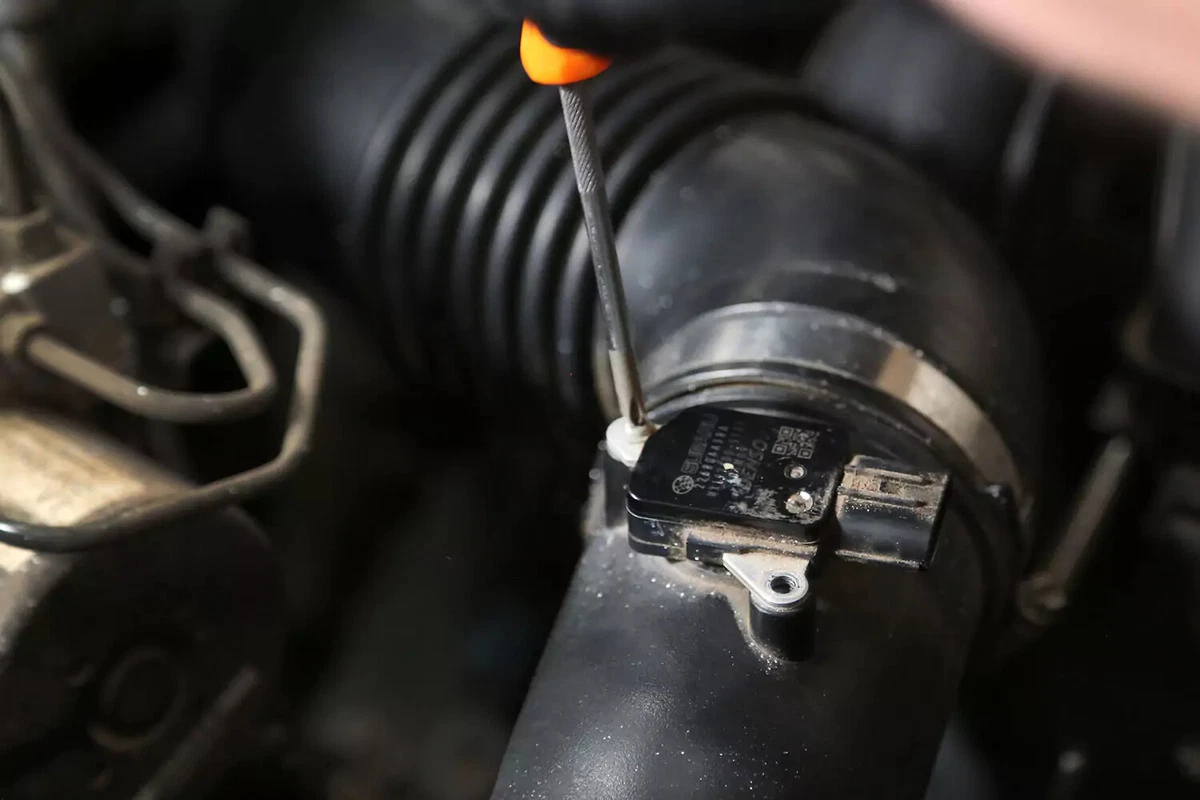 A screwdriver removing a screw on an engine MAF sensor.