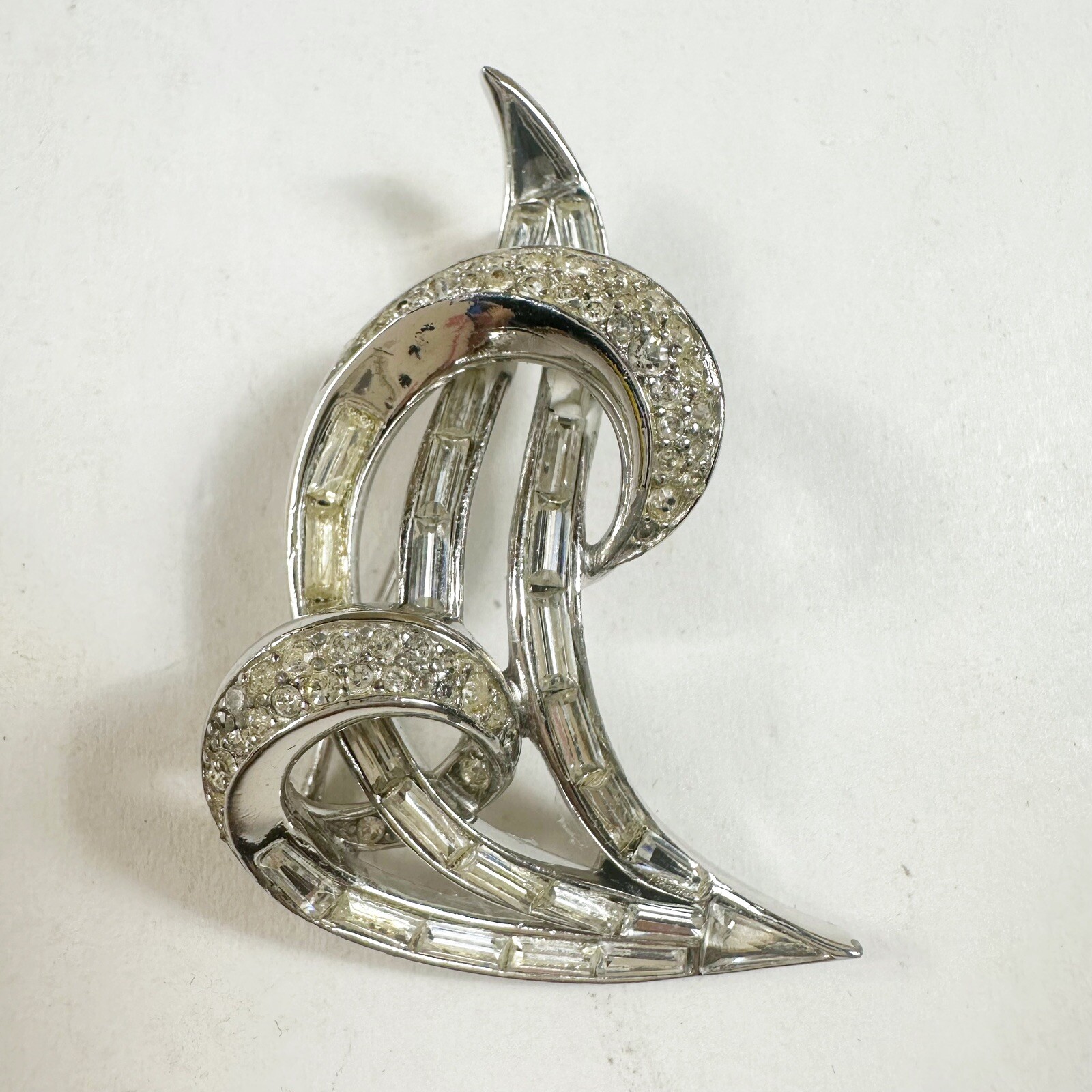 Silver tone Crown Trifari swirl-shaped brooch set with clear rhinestones