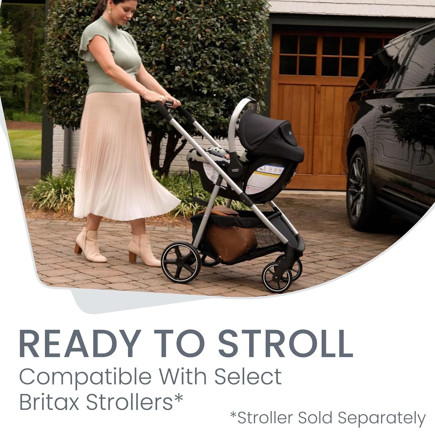 Woman pushing black and silver Britax Willow SC stroller with car seat, brown garage door and green hedge in background.