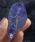 Rough purple zircon 411.05 ct with visible inclusions in metallic blue matrix, held by hand against gray background.