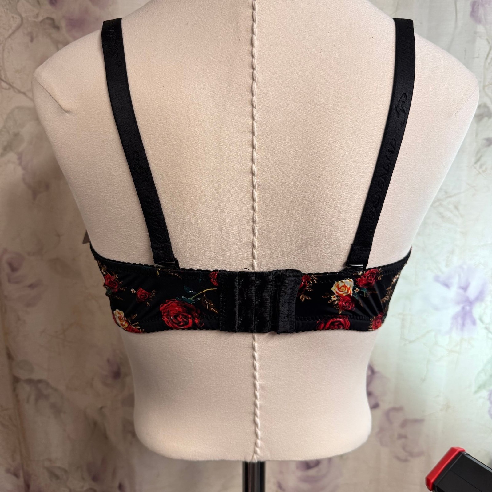 Black padded underwire bra with pink rose floral pattern and adjustable straps displayed on a dress form.