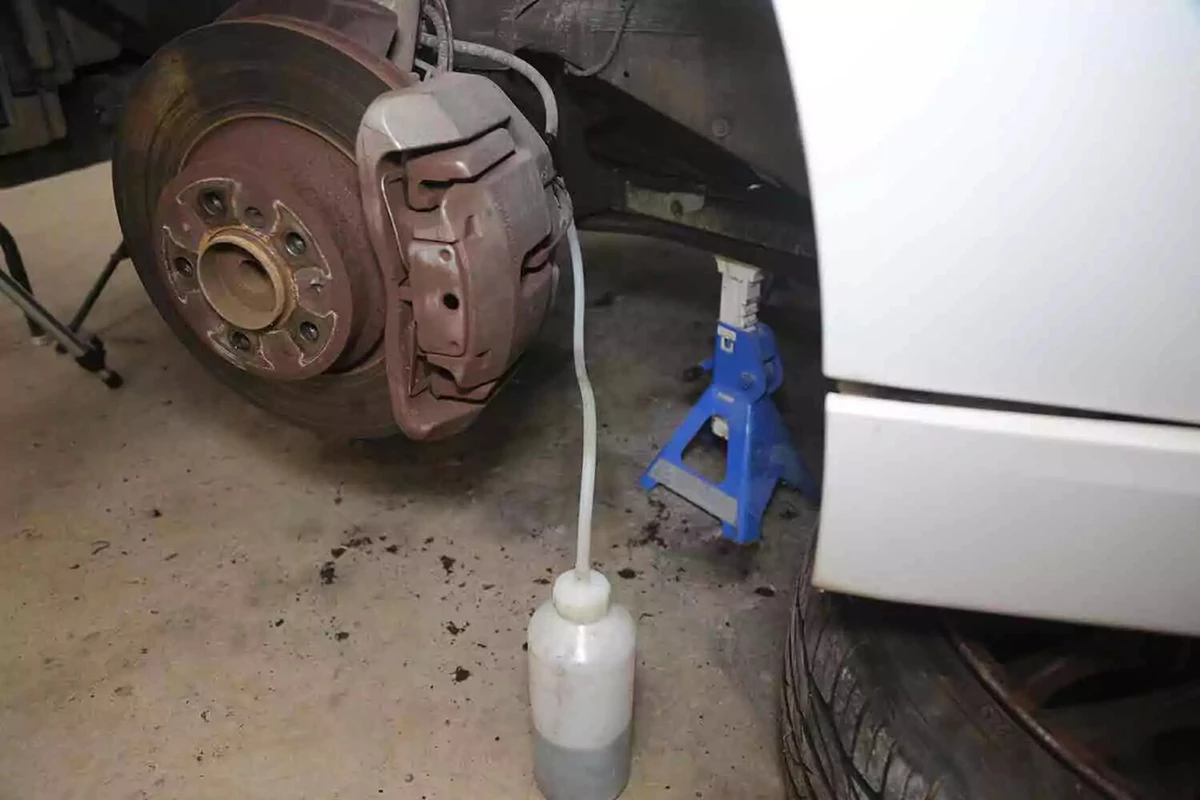 A brake bleeder kit's catch bottle sits on the ground with a hose leading to a vehicle's brake bleeder.