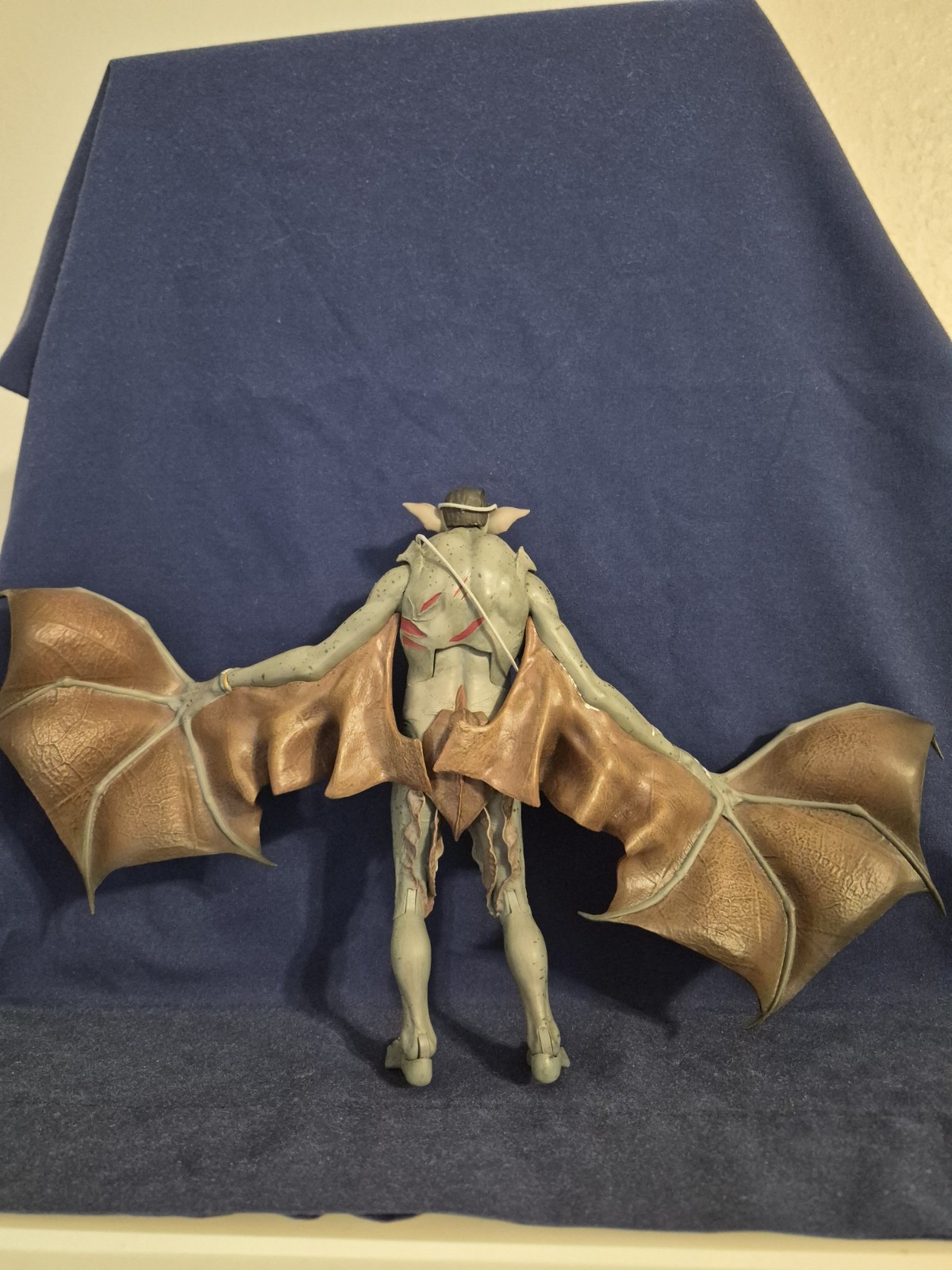 DC Collectibles Batman Arkham figure with bat wings, silver body, and red shoulder accents on blue fabric background.