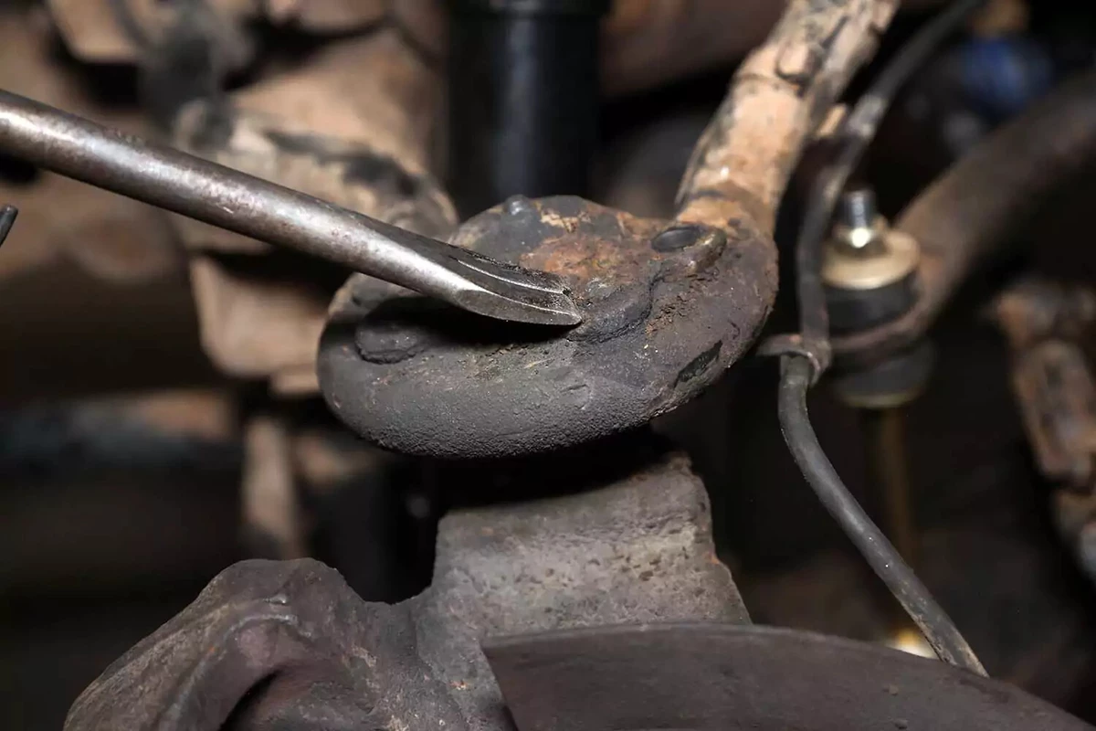 A mechanic uses a chisel to remove the rivet heads from the top of the ball joint.