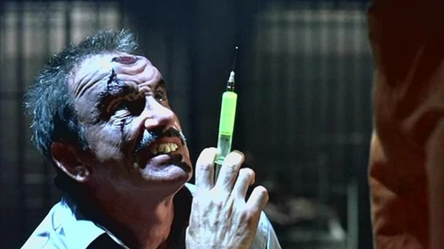 Man in white coat holding green syringe with yellow liquid, face close-up showing scars and veins.