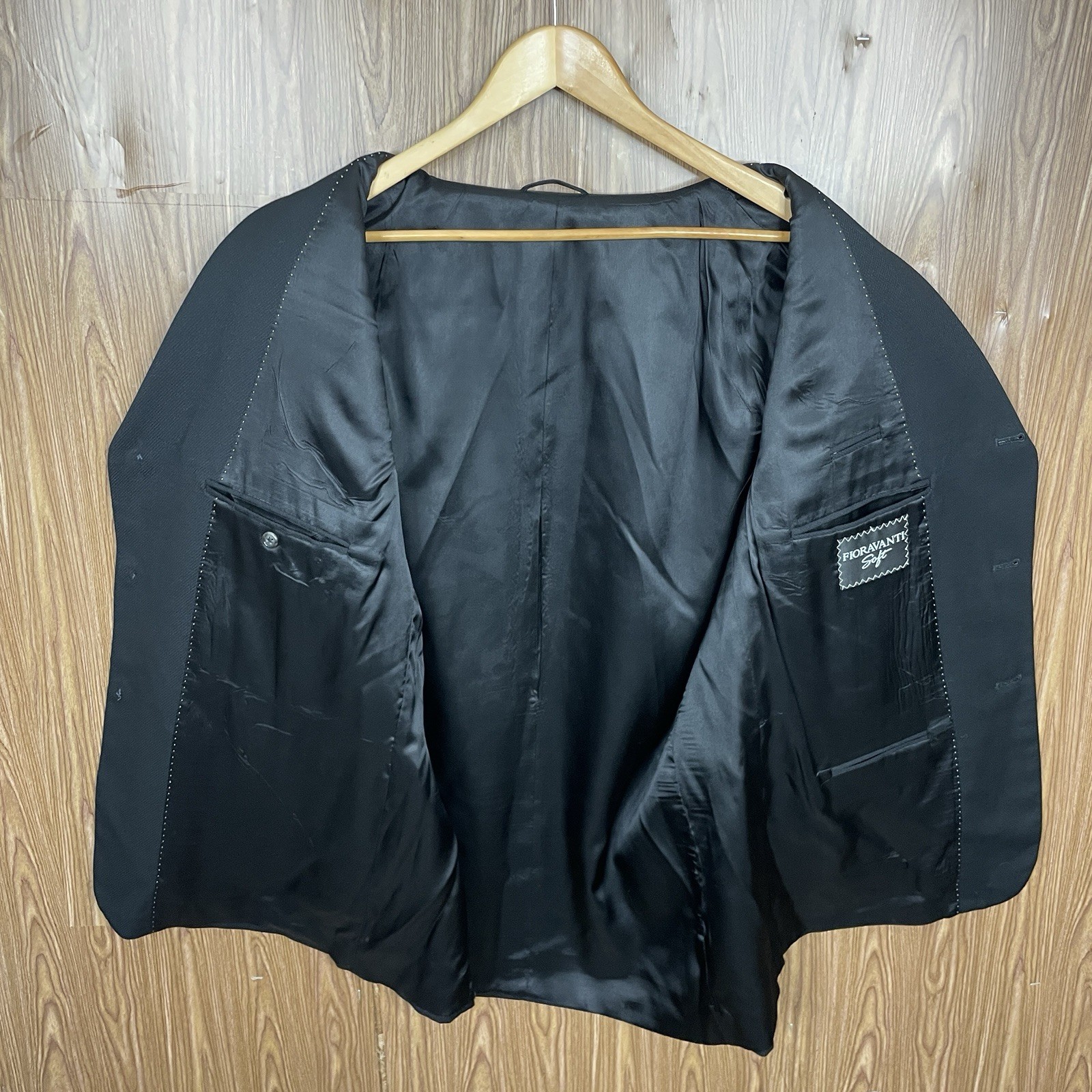 Black solid three-button blazer jacket with notch lapels, front flap pockets, and subtle textured fabric on hanger.