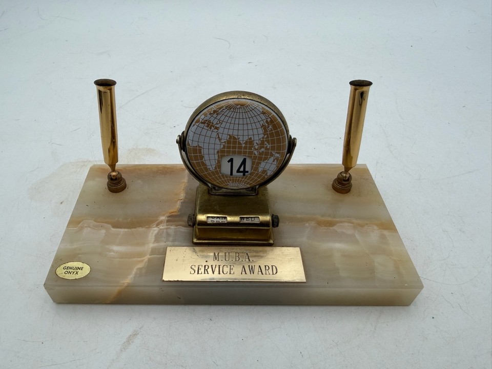 A perpetual globe calendar in onyx and brass with dual pen holders — analog time-keeping that looks like a prop from a Bond villain's study.