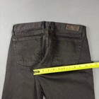 Black faded bootcut jeans with back pocket stitching and brown leather patch on waistband, measured against yellow tape.